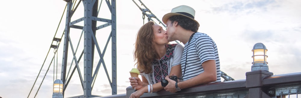 A man and woman kiss while standing on a bridge
