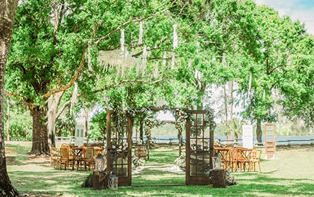 A canopy of trees provide shade over seating for an outdoor wedding