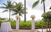 A table with candles and 2 flower stands grace a patio overlooking the ocean