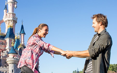 A man pulls a laughing woman towards him by Sleeping Beauty Castle